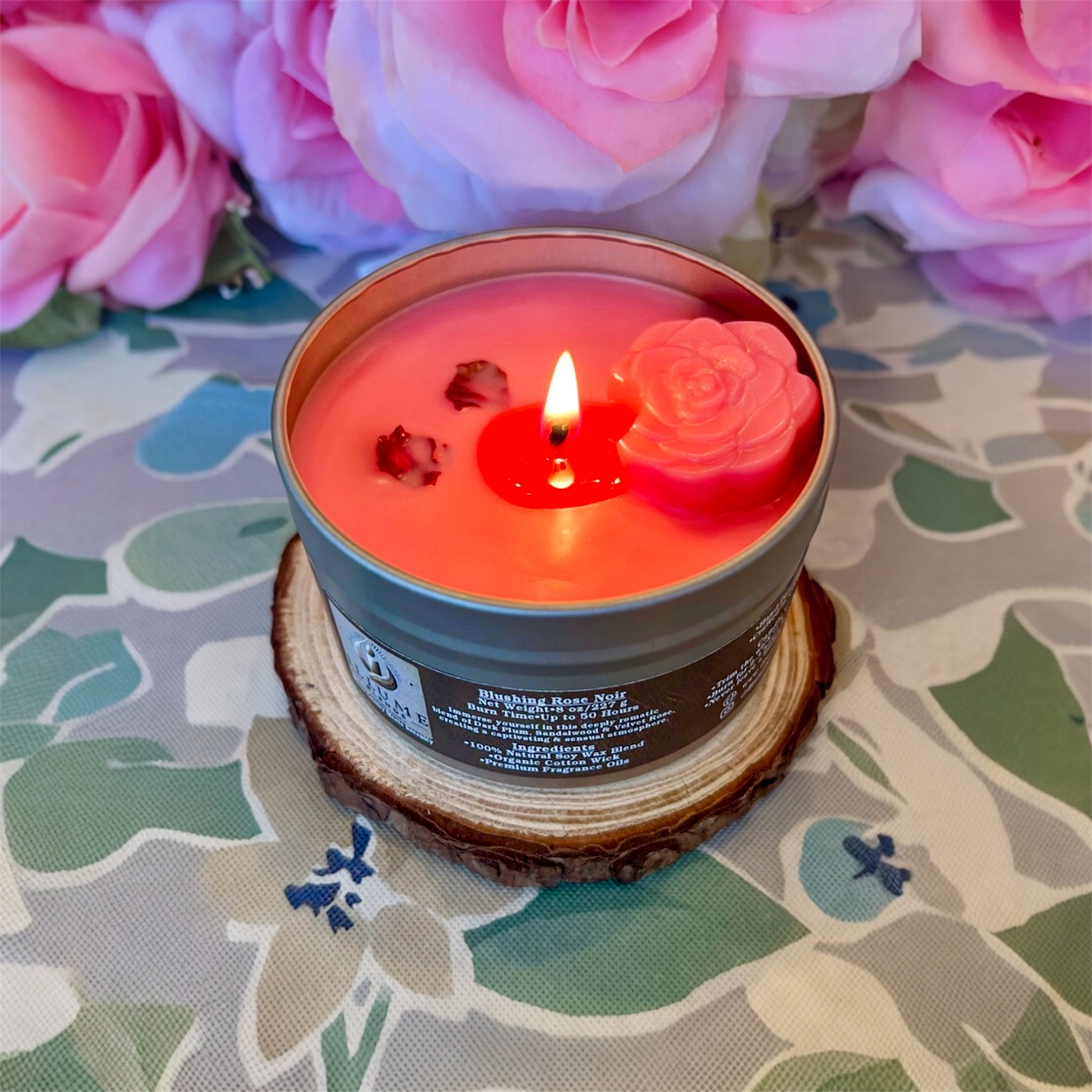 Lit Blushing Rose Noir candle with warm flame, rose wax embed, and romantic blush-toned wax in reusable tin