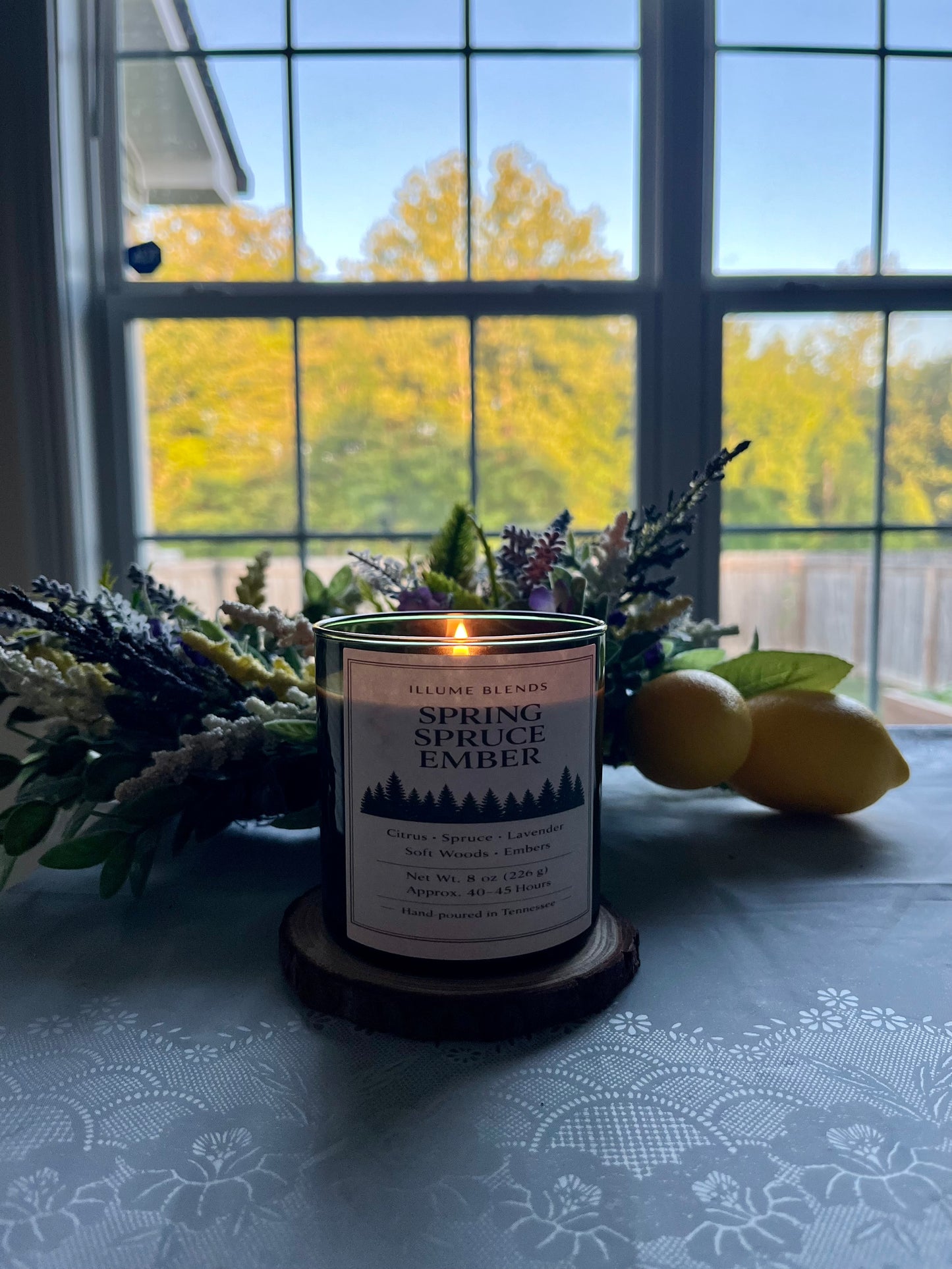 Spring Spruce Ember candle glowing beside a window at sunrise.