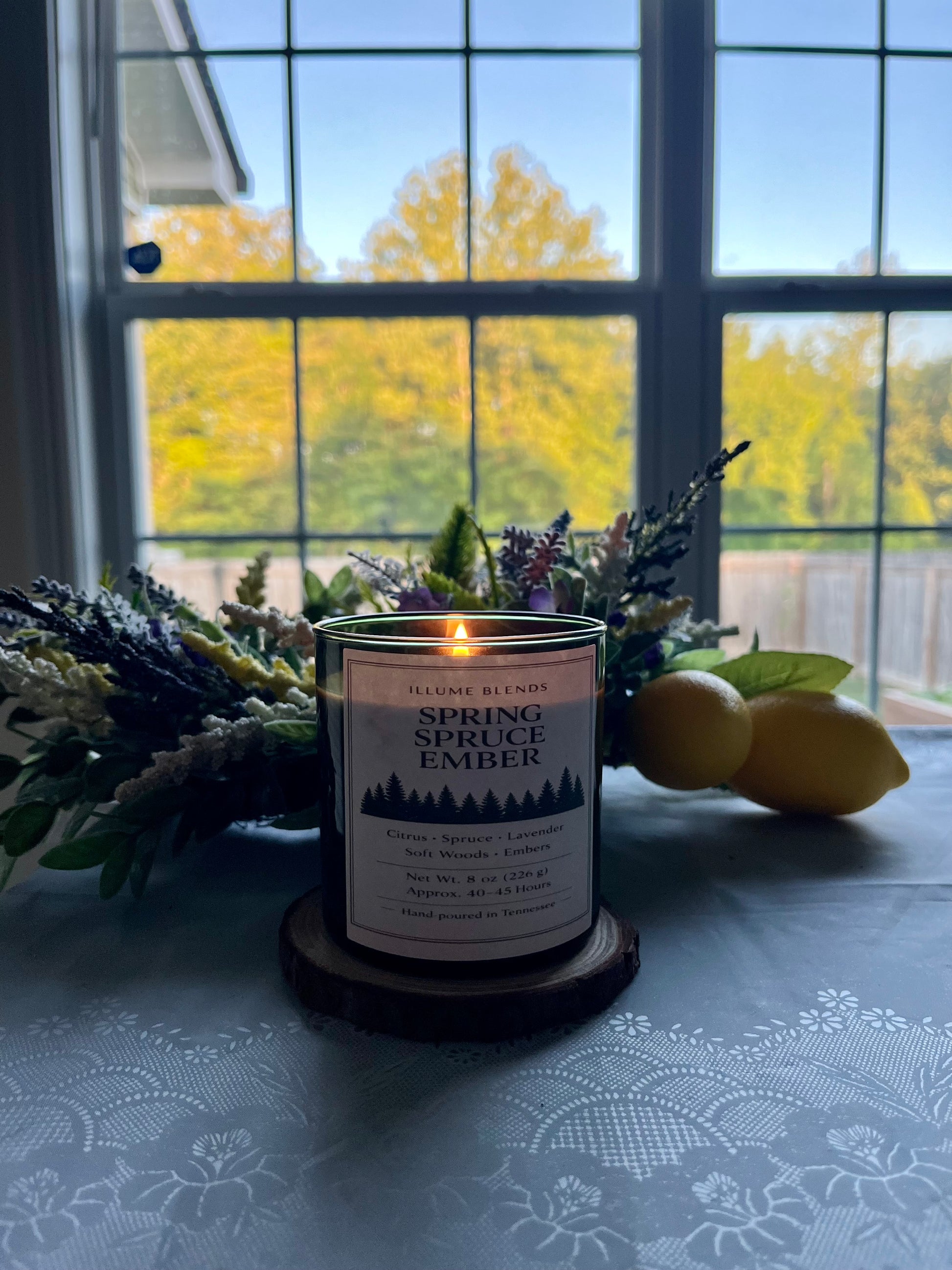 Spring Spruce Ember candle glowing beside a window at sunrise.